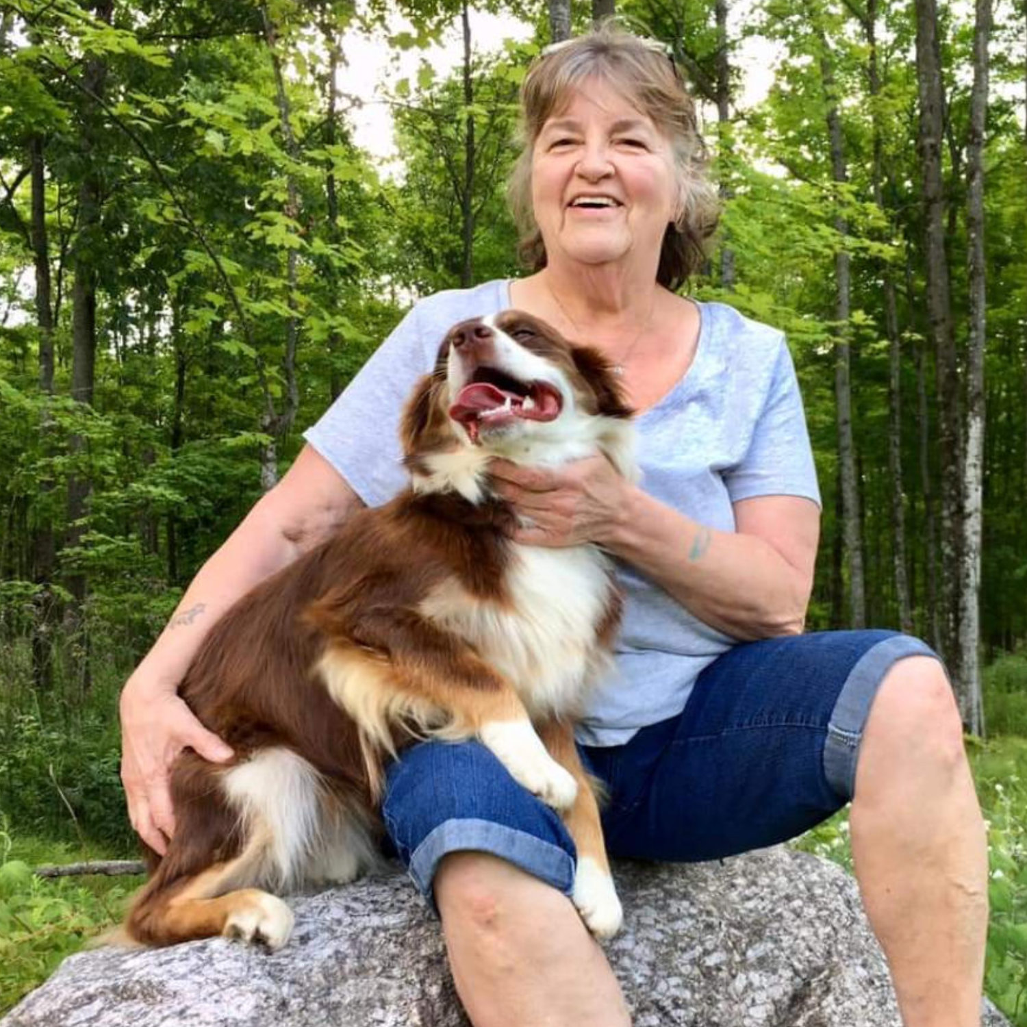 Deb Claus with dog in lap sitting on rock